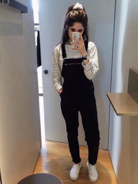 a young woman taking a selfie in front of a mirror wearing overalls and white sneakers