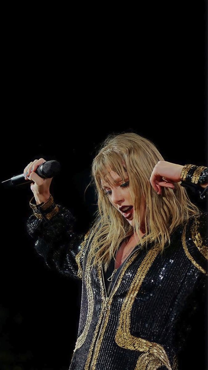 a woman with long blonde hair holding a microphone in her right hand and singing into the microphone