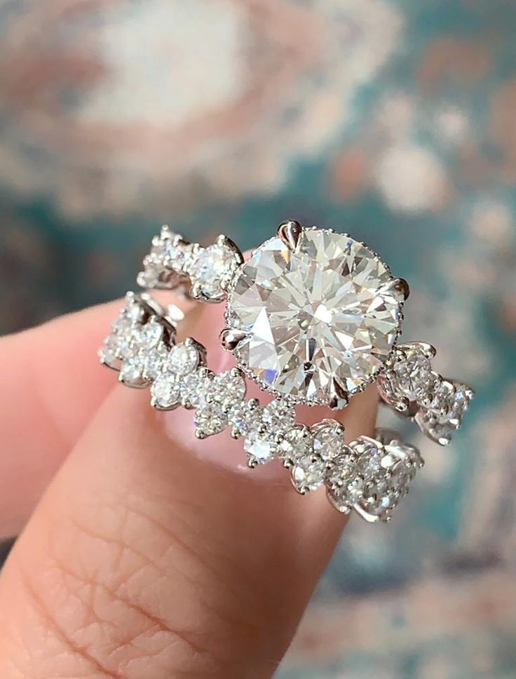 a woman's hand holding an engagement ring with diamonds on the band and side stones