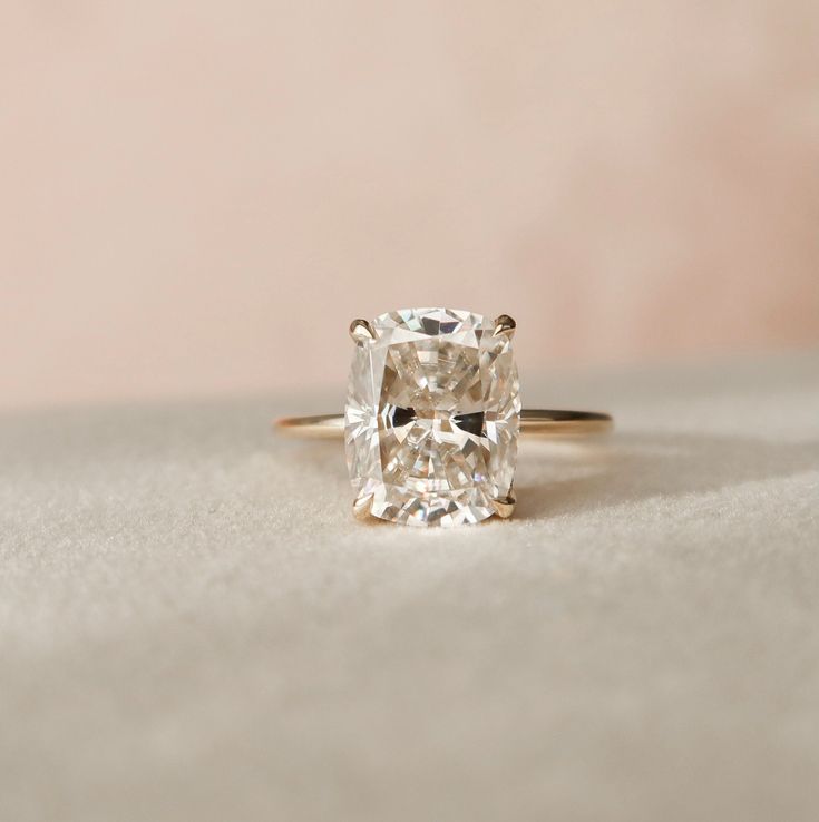 an engagement ring with a cushion cut diamond in the center, sitting on a white surface