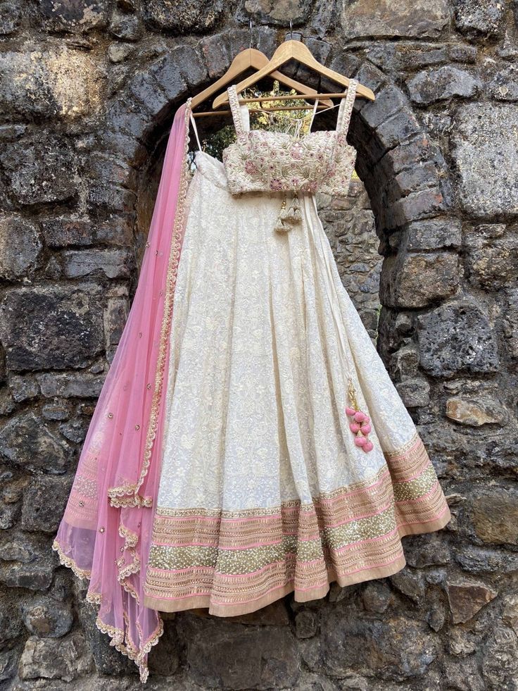 This stunning ivory Lucknowi thread work georgette lehenga is embellished with heavy gota, sequin, pearl and zari work border in pink accent. It is paired with a bustier in raw silk with mirror, zardozi and thread zardozi work all over. Lucknowi Lehenga, Embroidered Bustier, Georgette Lehenga, Work Lehenga, Floral Bustier, Pearl Embroidery, Zari Work, Net Dupatta, Pink Tulle