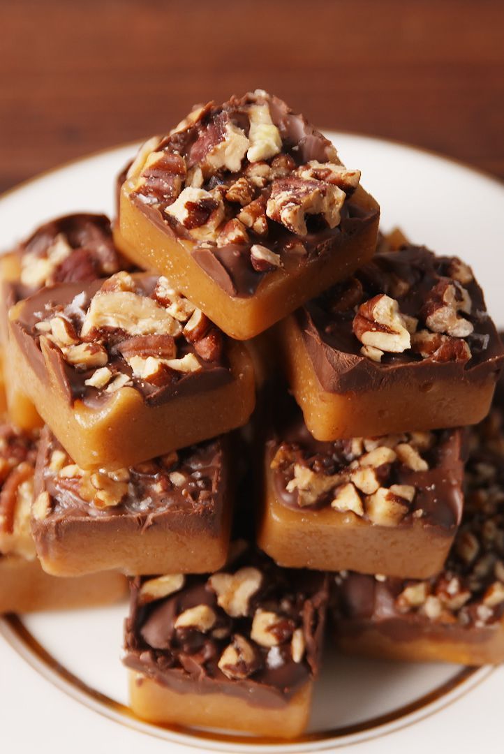 a white plate topped with lots of brownies covered in nuts and caramels