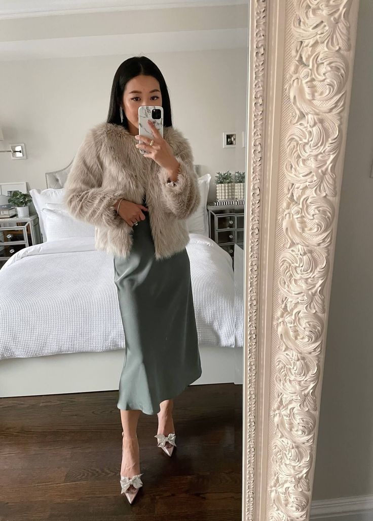 a woman taking a selfie in front of a mirror wearing a fur coat and slip ons