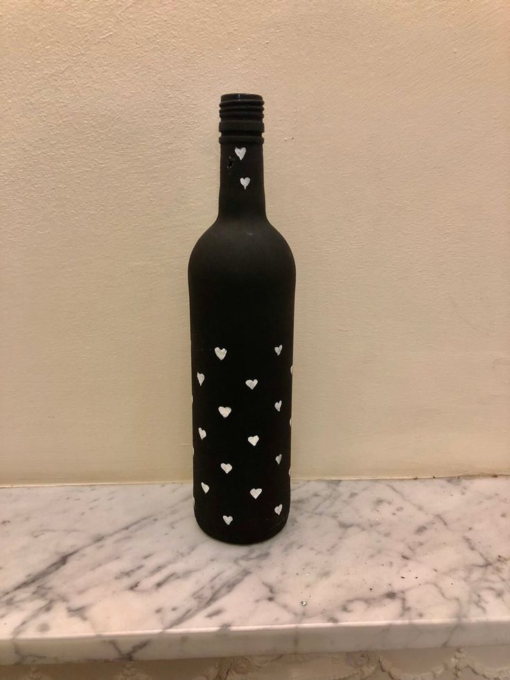 a black bottle with white hearts on it sitting on a marble counter next to a wall