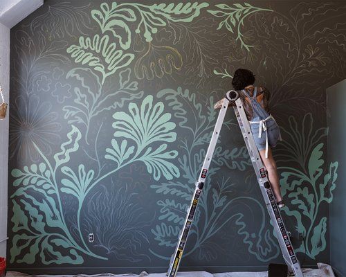 a man on a ladder painting a wall