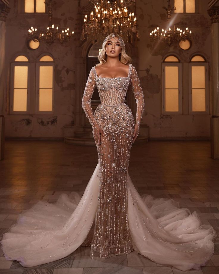 a woman in a long sleeved dress standing in front of a chandelier