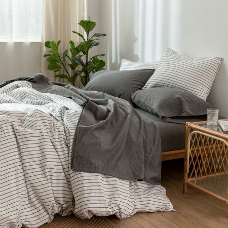 an unmade bed with grey and white linens in a small room next to a window