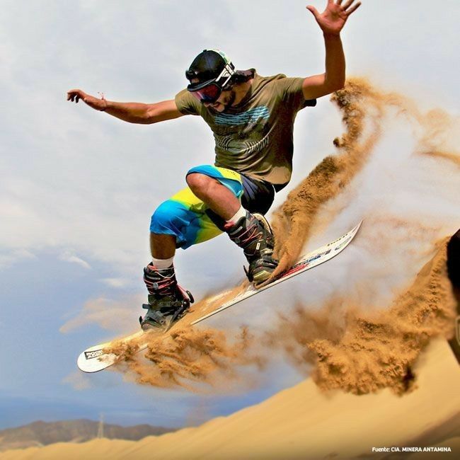 a man riding a snowboard down the side of a sand dune covered in dirt