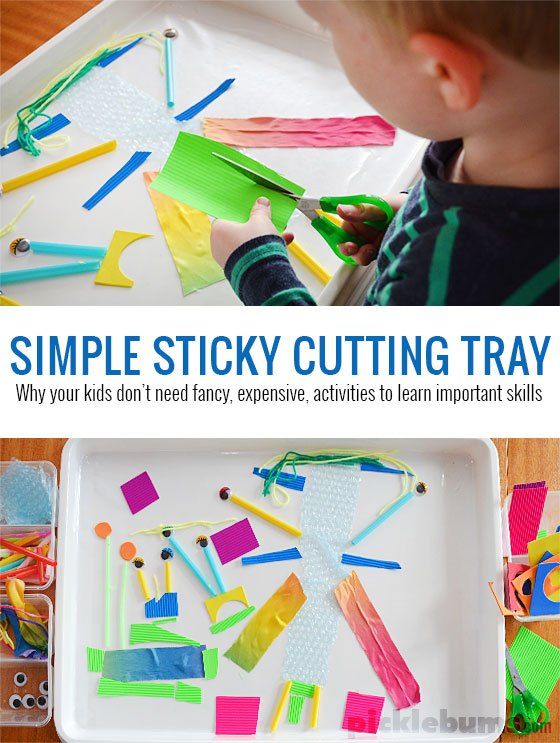 an image of a child cutting paper with scissors and glue on the tray that is filled with crafting materials