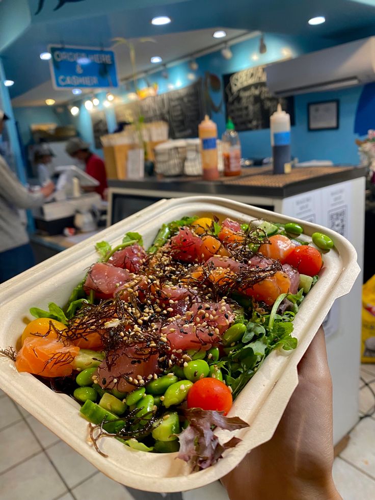 a person holding up a plastic container filled with vegetables and meat on top of it