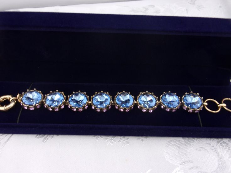 A truly eye-catching and elegant vintage piece in beautiful condition with an amazing sparkle! Beautiful and unique one-of-a kind design. The rhinestone bracelet is made up of eight blue topaz round cut faceted stones that measure 5/8", approximately the size of a dime. They are set in a goldtone metal surrounded at the base with small purple rhinestones.  The stones are securely set in a goldtone metal setting with no loose or missing stones. All have a brilliant sparkle! Will be packaged in a lovely blue velvet gift box as shown and ready for gift giving. For other vintage jewelry listings please visit:  https://www.etsy.com/shop/DreamofjeanieDesigns?ref=seller-platform-cnav&section_id=23284464 Jeweled Bracelets For Formal Occasions, Elegant Formal Topaz Bracelets, Elegant Formal Topaz Bracelet, Formal Jeweled Crystal Bracelets, Blue Round Crystal Bracelet For Formal Occasions, Blue Crystal Bracelet For Formal Occasions, Formal Blue Round Crystal Bracelet, Formal Crystal Bracelet With Stones, Costume Jewelry Bracelet With Sparkling Stones For Formal Occasions