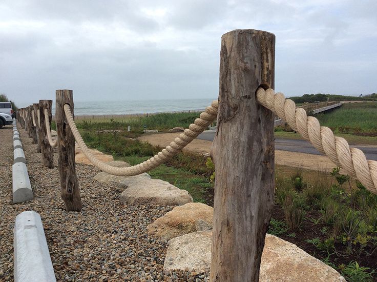 a wooden post with rope attached to it next to the beach and ocean in the background