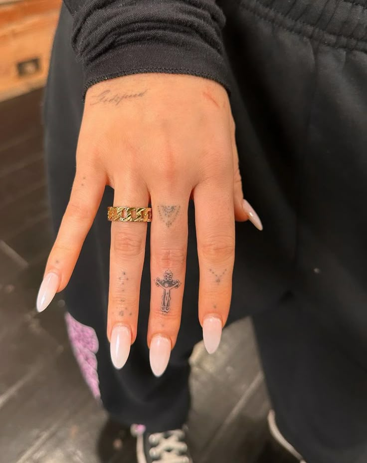 a woman's hand with tattoos on it and a cross tattoo on the middle finger