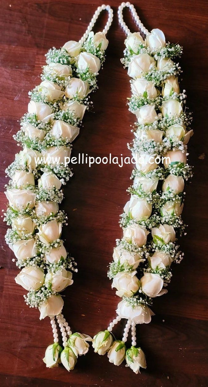 white roses and baby's breath are arranged on a wooden table with pearls in the middle