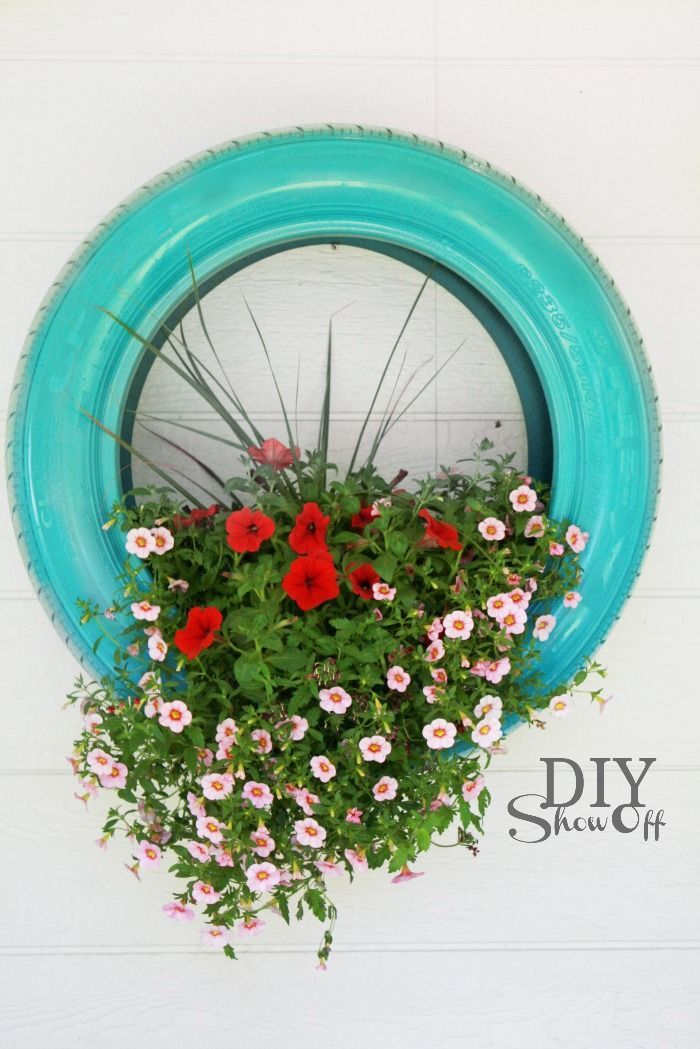 a blue tire hanging from the side of a wall with flowers in it and grass growing inside