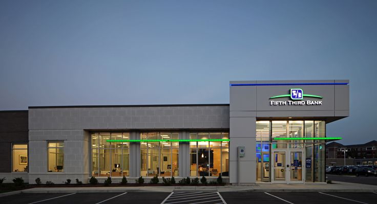 an empty parking lot in front of a building with lights on at the entrance to it