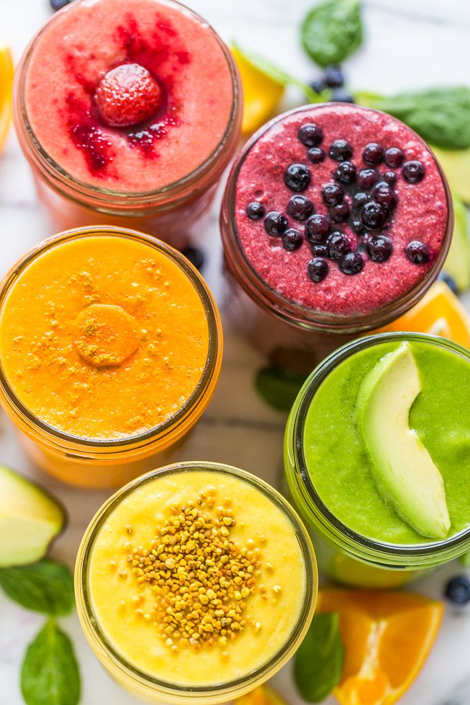 four different smoothies in small glass cups with fruit and vegetables on the side, top view