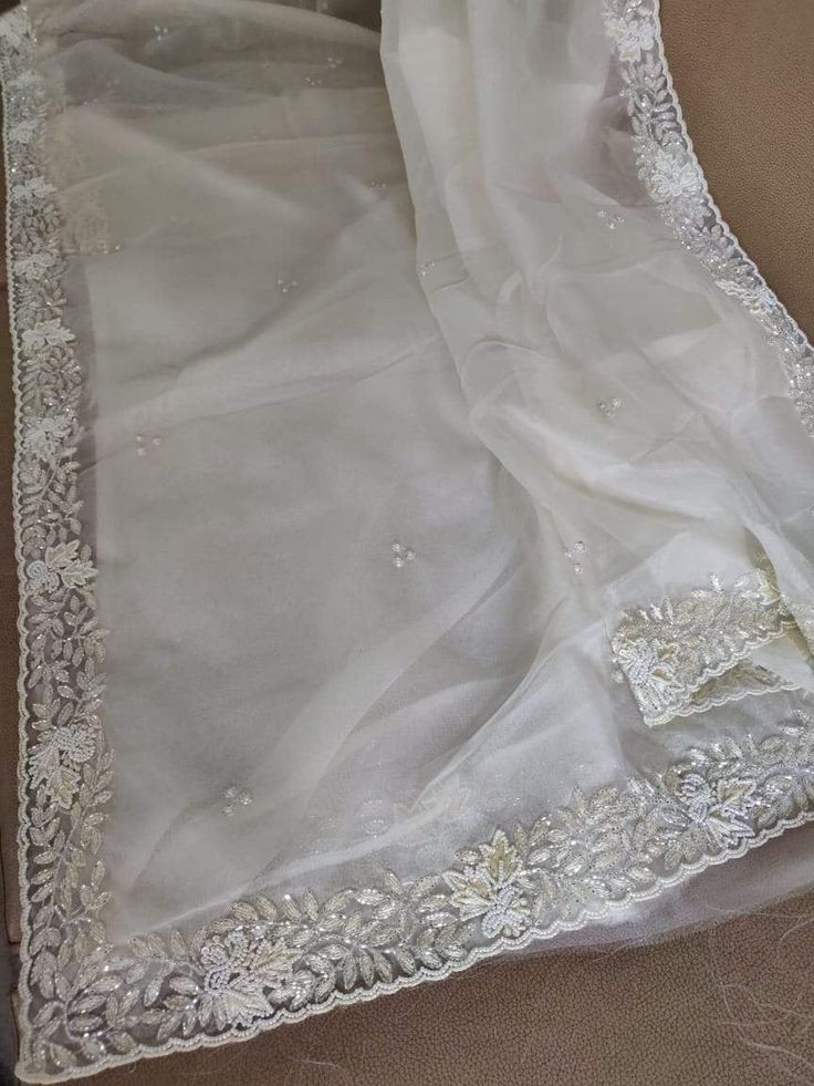 This is a fascinating pure organza silk saree in gorgeous white color, monochrome look. Saree features a dazzling beads and pearl work embroidery of floral design throughout the edges of the saree. Simple pearl work is twinkling all over the body of the saree. The beads and pearl embroidery are delicately hand embellished. Organza is a lightweight plain weave fabric. The pure organza attributes to a very comfy and flowy drape. Organza is considered as one of the most stylish and glamorous wear. Semi-stitched White Organza Saree, Elegant Off White Dupatta In Traditional Drape, Elegant Off White Traditional Dupatta, Elegant Organza Blouse Piece, Elegant Off White Silk Dupatta, Elegant Off-white Silk Dupatta, Organza Saree With Pearl Embroidery For Party, Elegant Organza Dupatta With Pearl Embroidery, Elegant Off White Saree With Cutdana