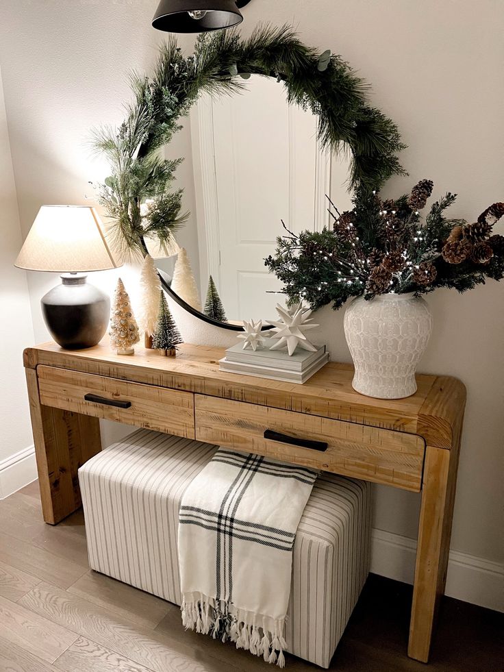 a wooden table topped with a mirror next to a white vase filled with greenery