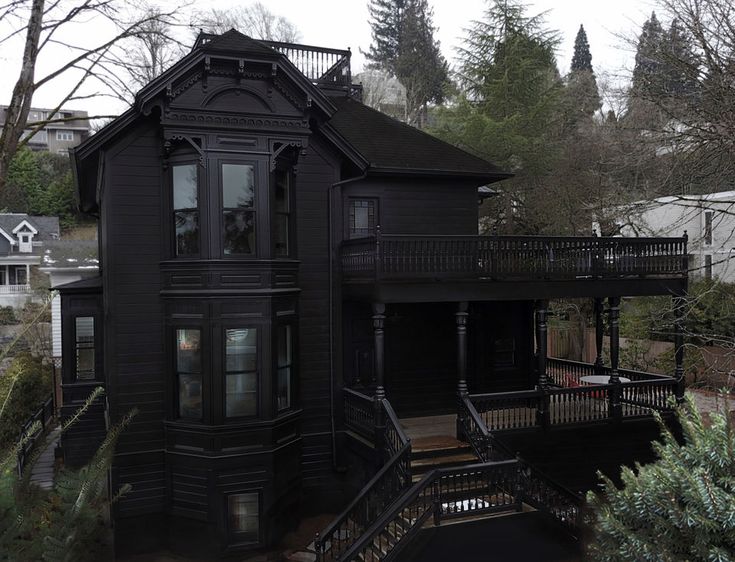 an old black house in the middle of some trees and houses with balconies