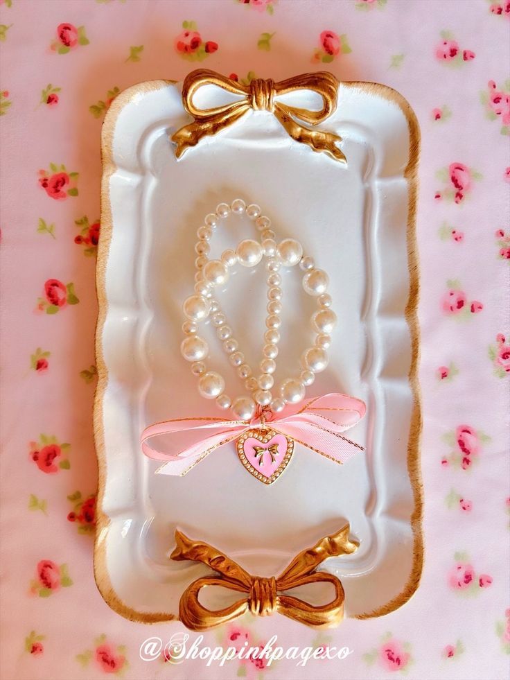 a white plate with pearls and a pink bow on it, next to a small pearl necklace