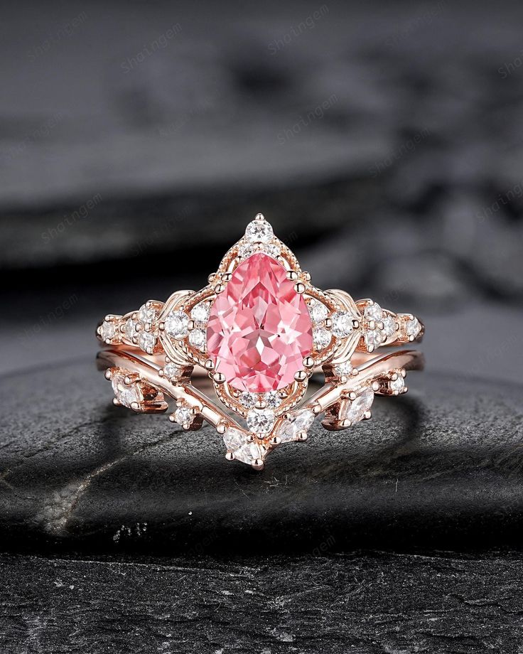 a pink diamond ring sitting on top of a black stone slab with white diamonds around it