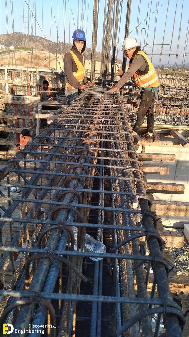 two men in hard hats and safety vests working on a steel beam at a construction site