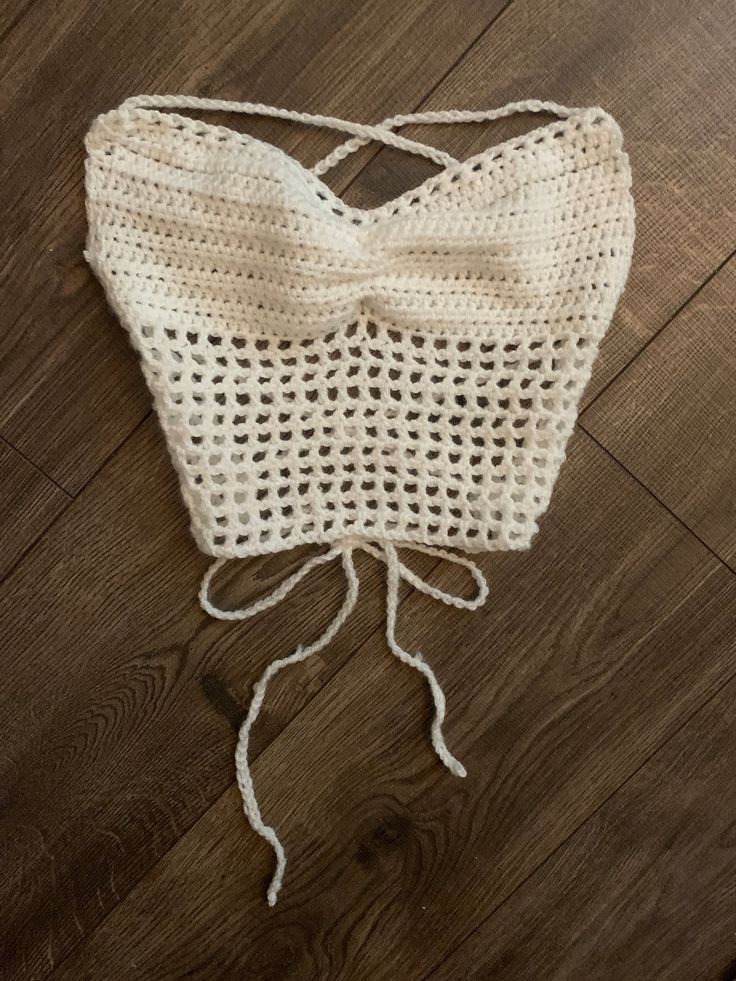 a white crocheted bag with a bow on the front and side, sitting on top of a wooden floor