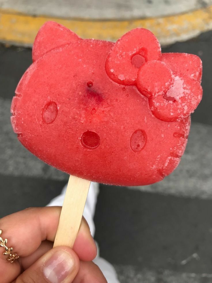 a hand holding a popsicle with hello kitty on it's end and gummy bears on top