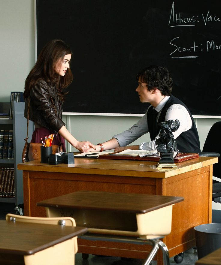 two people standing at a desk in front of a blackboard