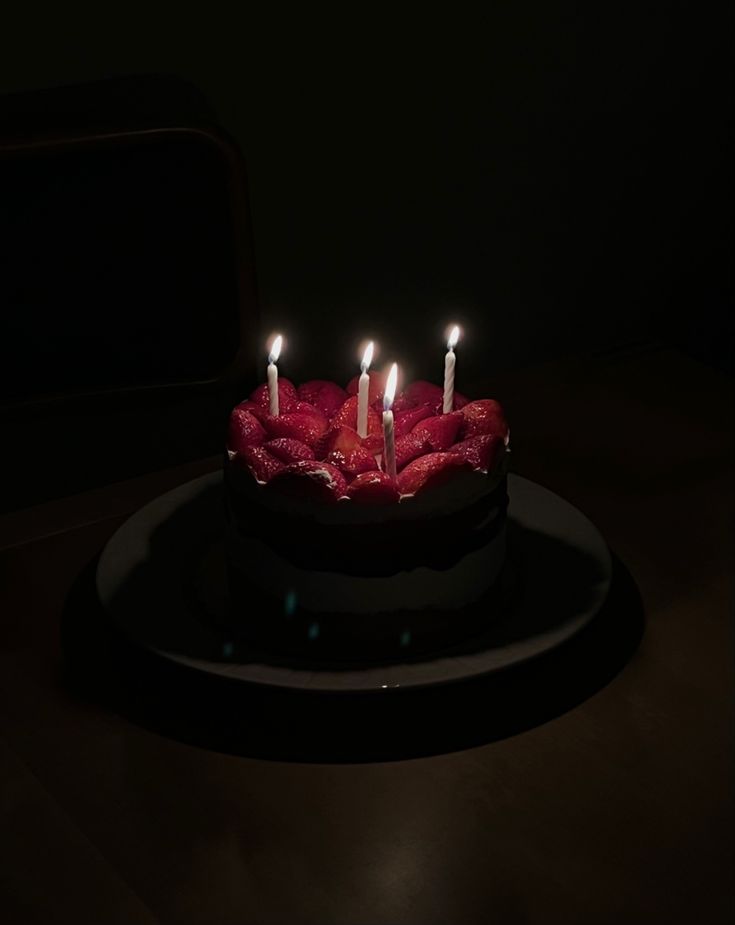 a birthday cake with lit candles sitting on a black plate in the middle of a dark room