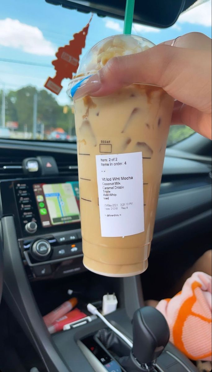 a person holding up a drink in their hand while sitting in the driver's seat