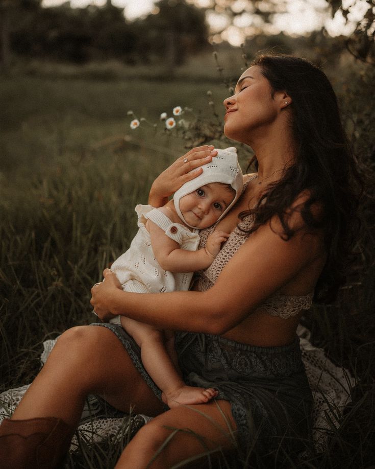 a woman holding a baby in her arms while sitting on the grass with daisies