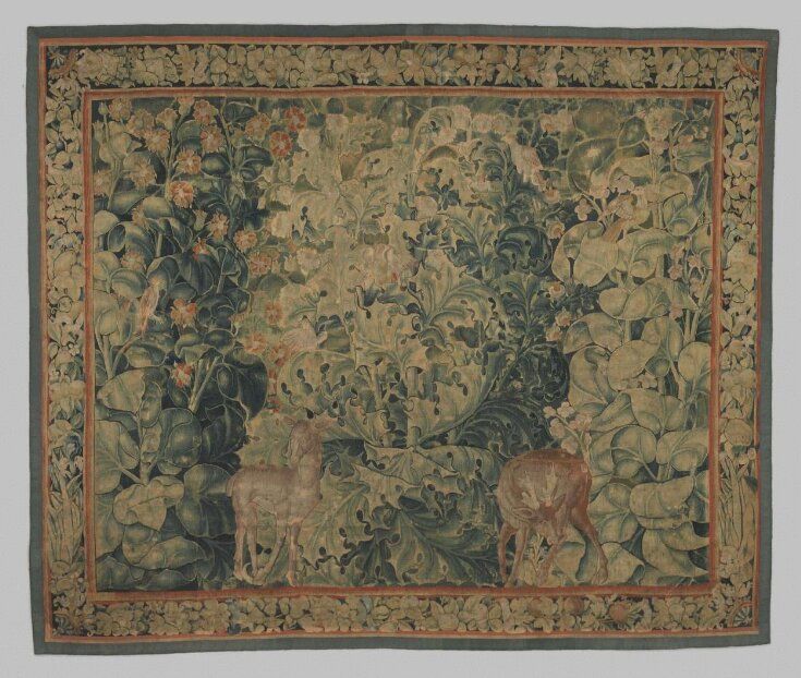 an old tapestry with deer and flowers on it's border, hanging from the wall