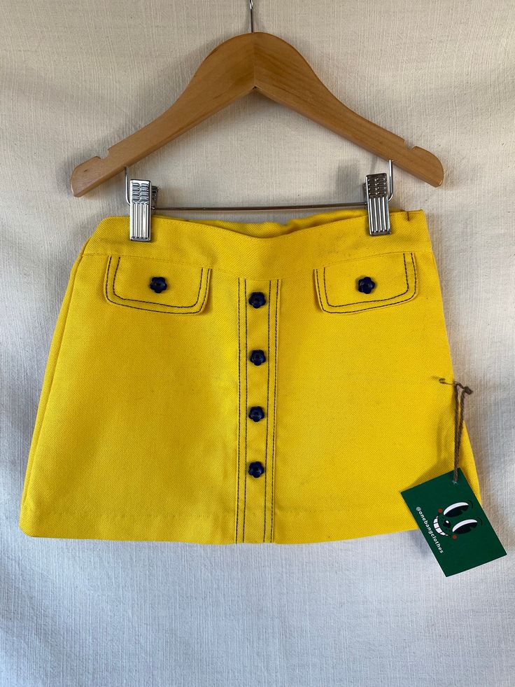 Short vintage 60s trapeze-style skirt in bright yellow, made of frame-style cotton fabric, with buttons and decorative pocket flaps on the front, in the shape of little navy blue flowers, the waistband has an internal elastic for easy putting on and taking off. The cut of the skirt, the contrasting seams in the same tone as the decorative flower buttons are a hymn to love and the flower power of the most hippie decade in history. This skirt, brought directly from London, is a new unsold stock garment and is in perfect condition except for a few small rust marks on the waistband because after all it is a piece that has more than 50 year of paitently waiting for an owner (please do feel free to ask for more photos and details of this). It is a very colorful and very swinging London garment, Retro School Bottoms For Spring, Retro Bottoms For School In Spring, Cotton School Skirt For Spring, Cotton Skirt For School In Spring, Cotton Skirt For School During Spring, Spring School Cotton Skirt, Spring Cotton Skirt For School, Retro Cotton School Bottoms, Retro Cotton Bottoms For School