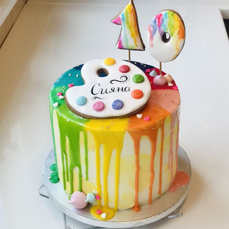 a birthday cake decorated with colorful icing and decorations on a white countertop next to a number one sign