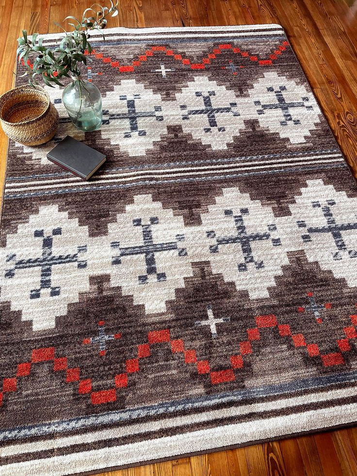 a brown and white rug on the floor next to a vase with flowers in it