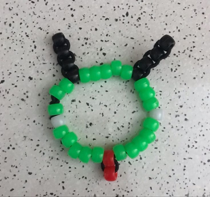 a green bracelet with black beads and red bead around it on a white surface