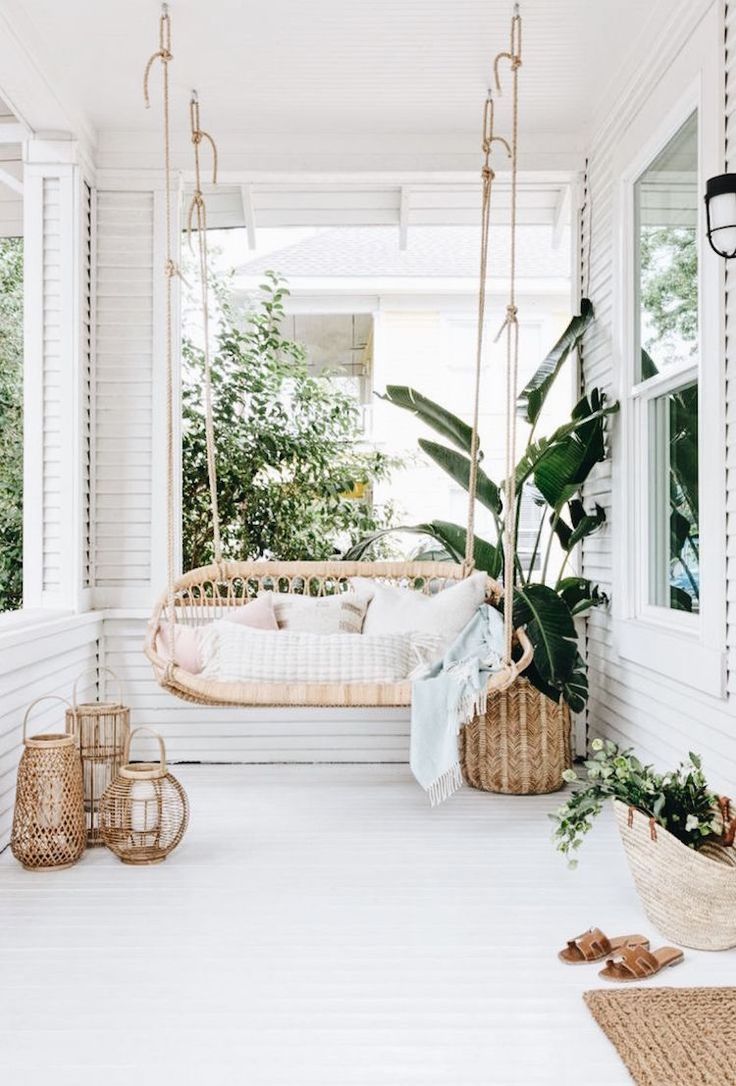 a white porch with some plants on it and hanging chairs in front of the door