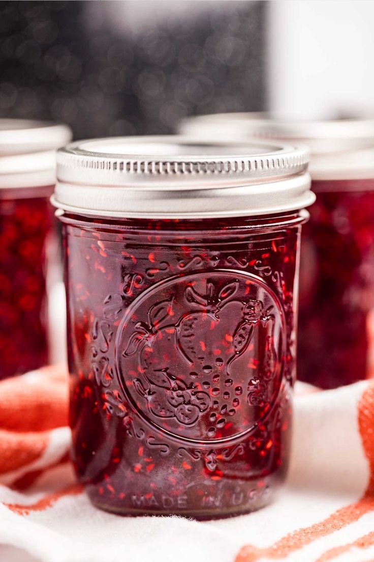 three jars filled with red liquid sitting on top of a white table cloth next to an orange towel