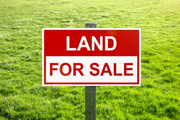 a red and white land for sale sign in the middle of a field with green grass