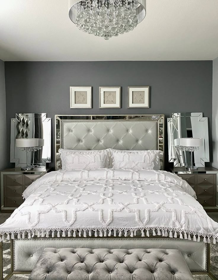 a white bed sitting under a chandelier next to two pictures on the wall