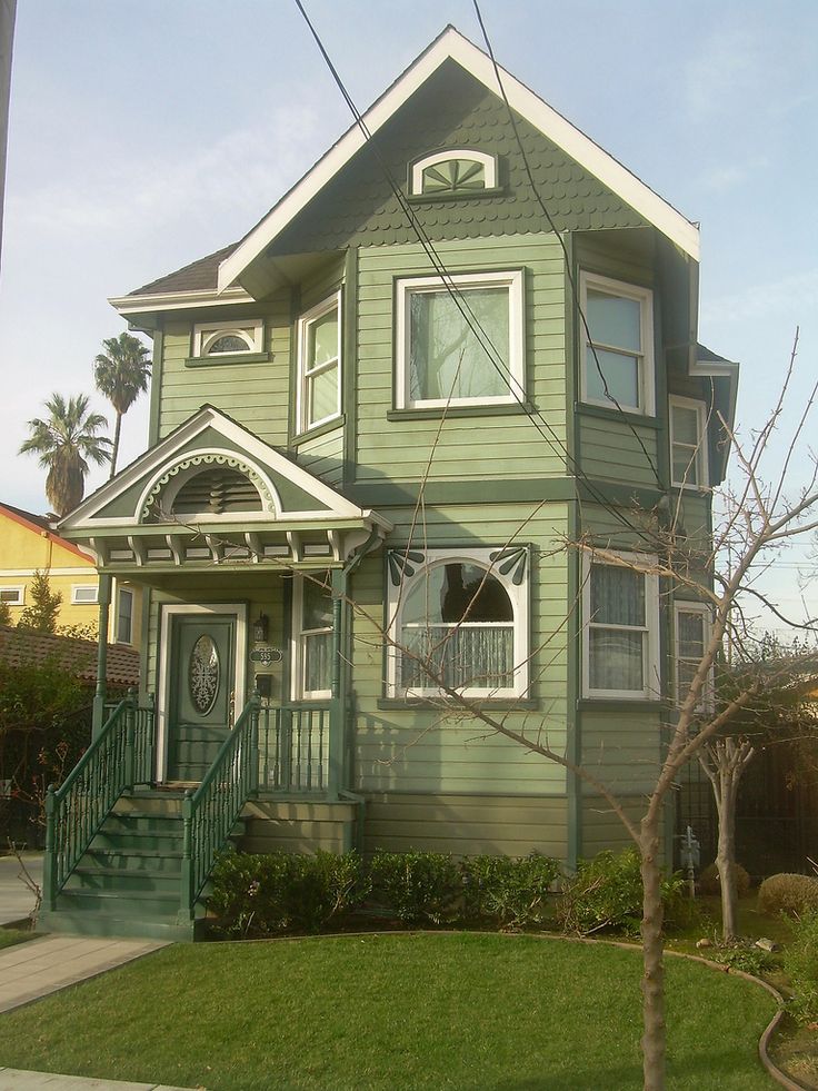 a green two story house with white trim on the front and second story, along side a tree