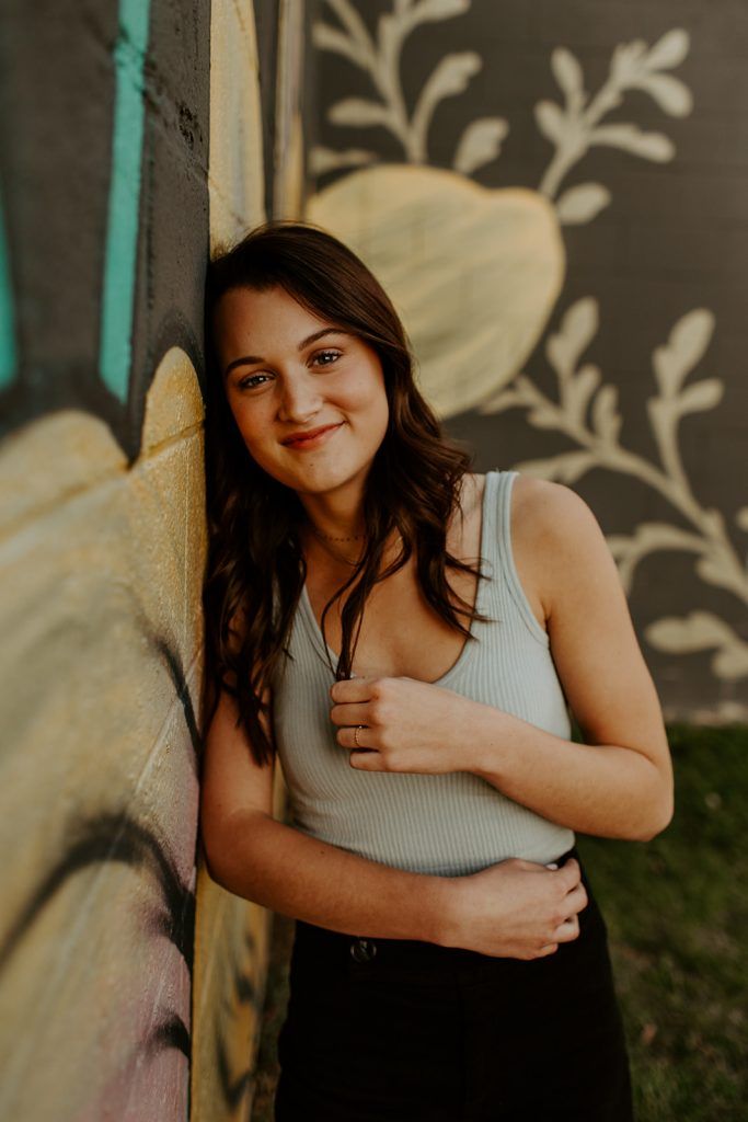 a young woman leaning against a wall with her arms around the back of her body