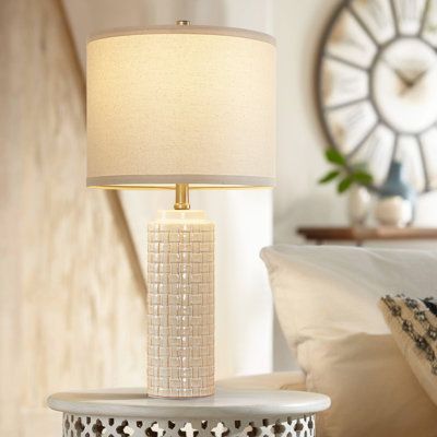 a white table lamp sitting on top of a night stand next to a bed with pillows