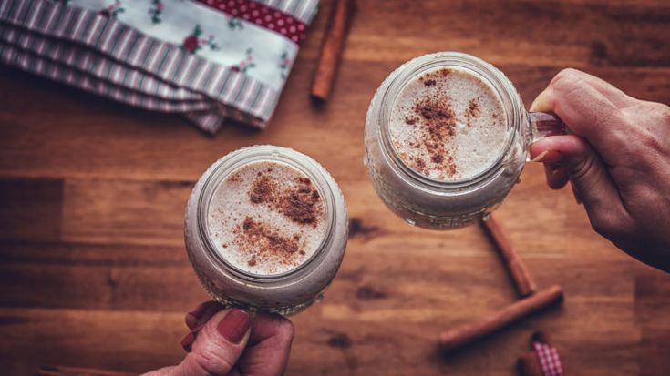 two people are toasting mugs with cinnamon on the top and one is filled with coffee