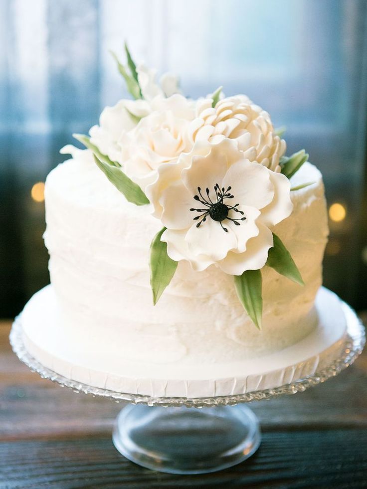 there is a white cake with flowers on the top and bottom tier, sitting on a glass plate