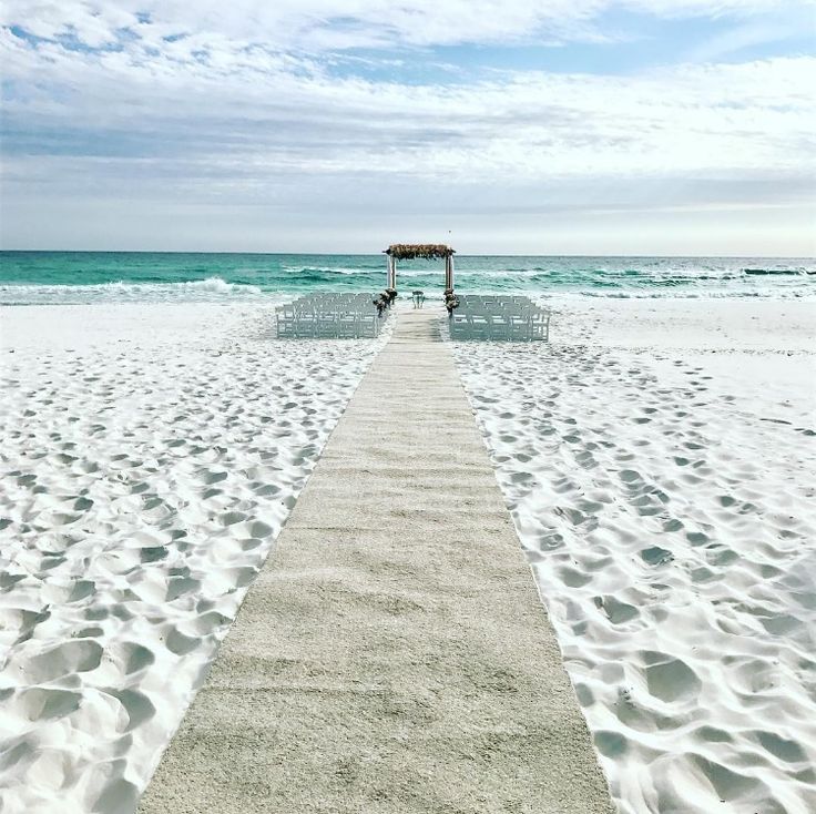 an empty walkway leading to the beach with chairs on it's sides and water in the background