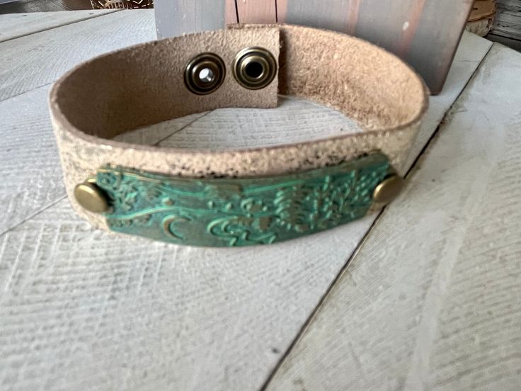 a leather bracelet with two metal buttons on top of white wooden planks next to a door