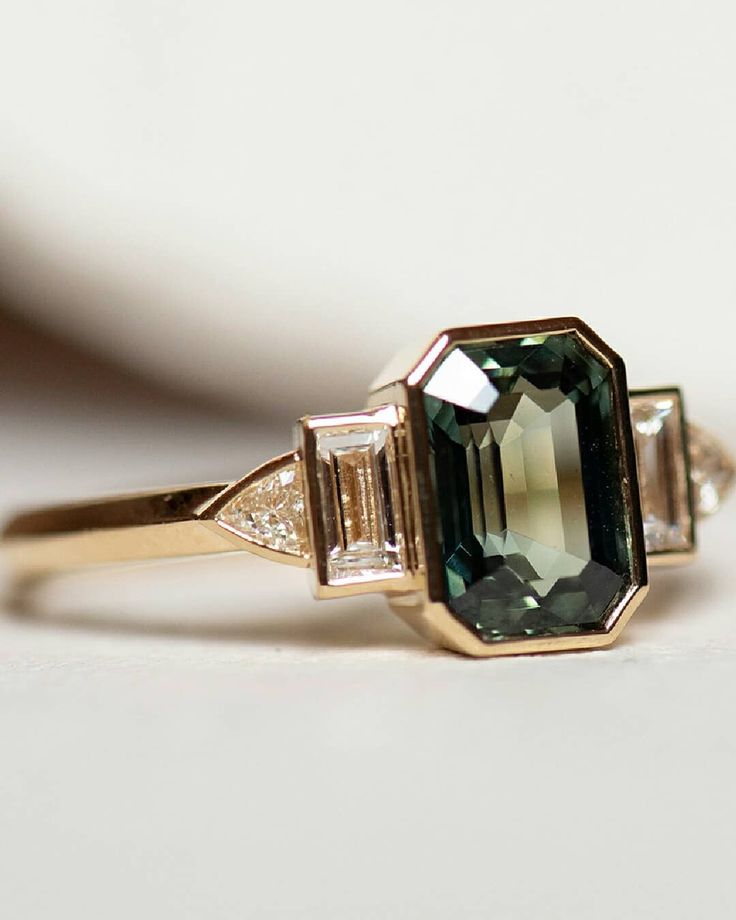 an emerald and diamond ring sitting on top of a table